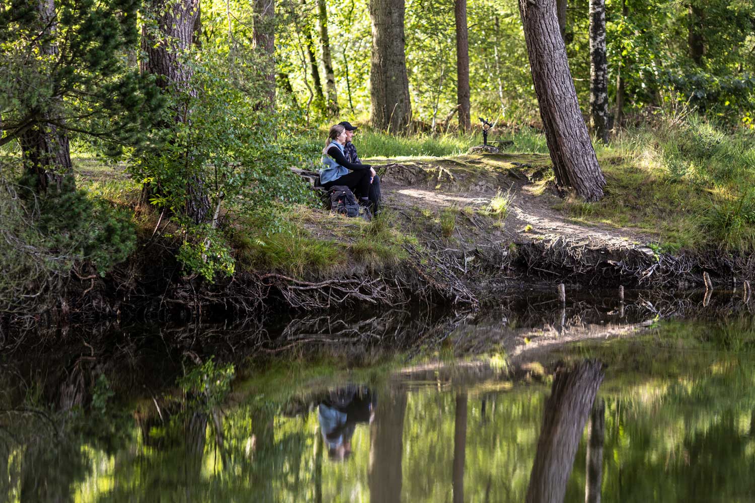 2 Wandernde sitzen an einem See im Wald