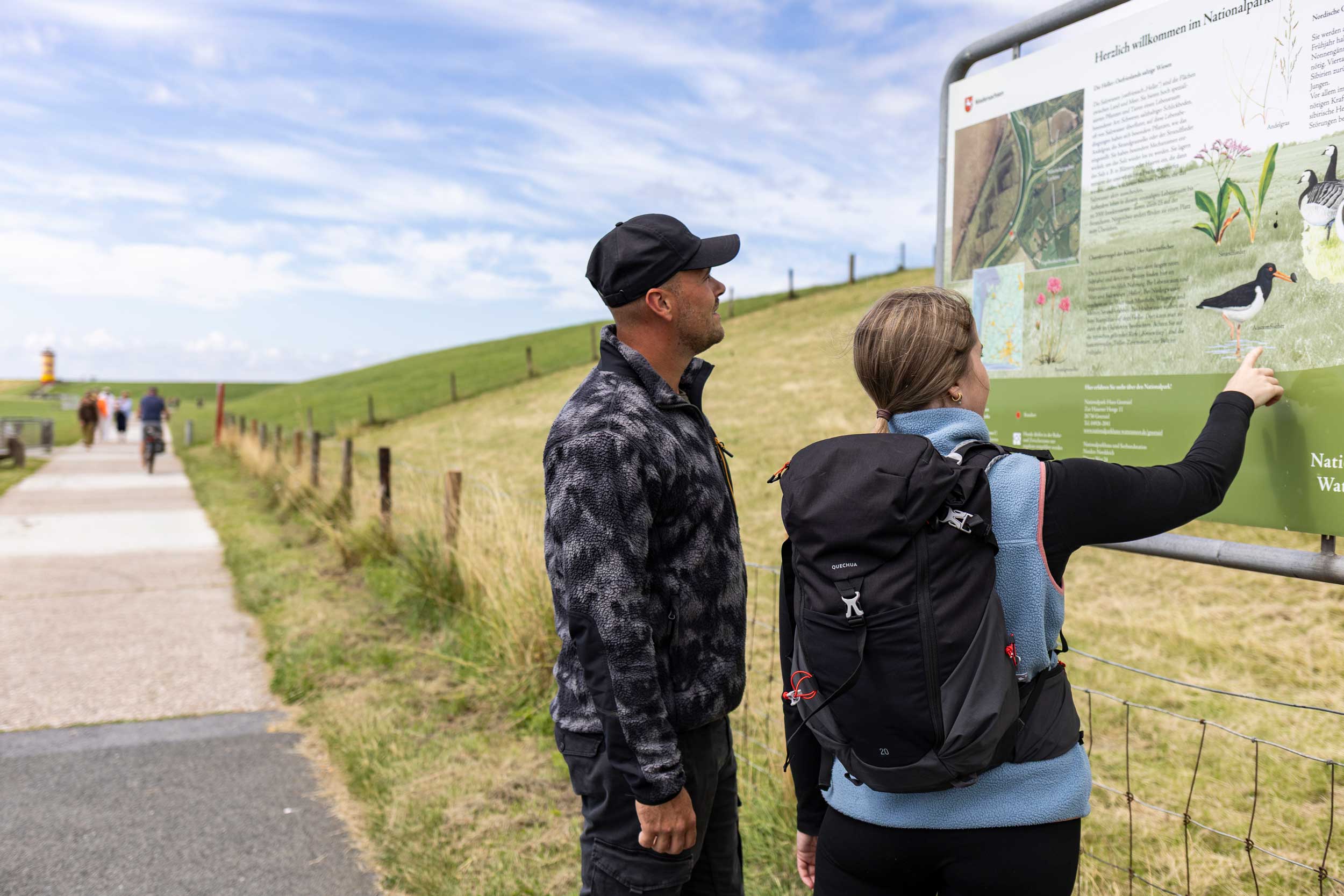 Zwei Wandernde am Deich schauen eine Informationstafel an
