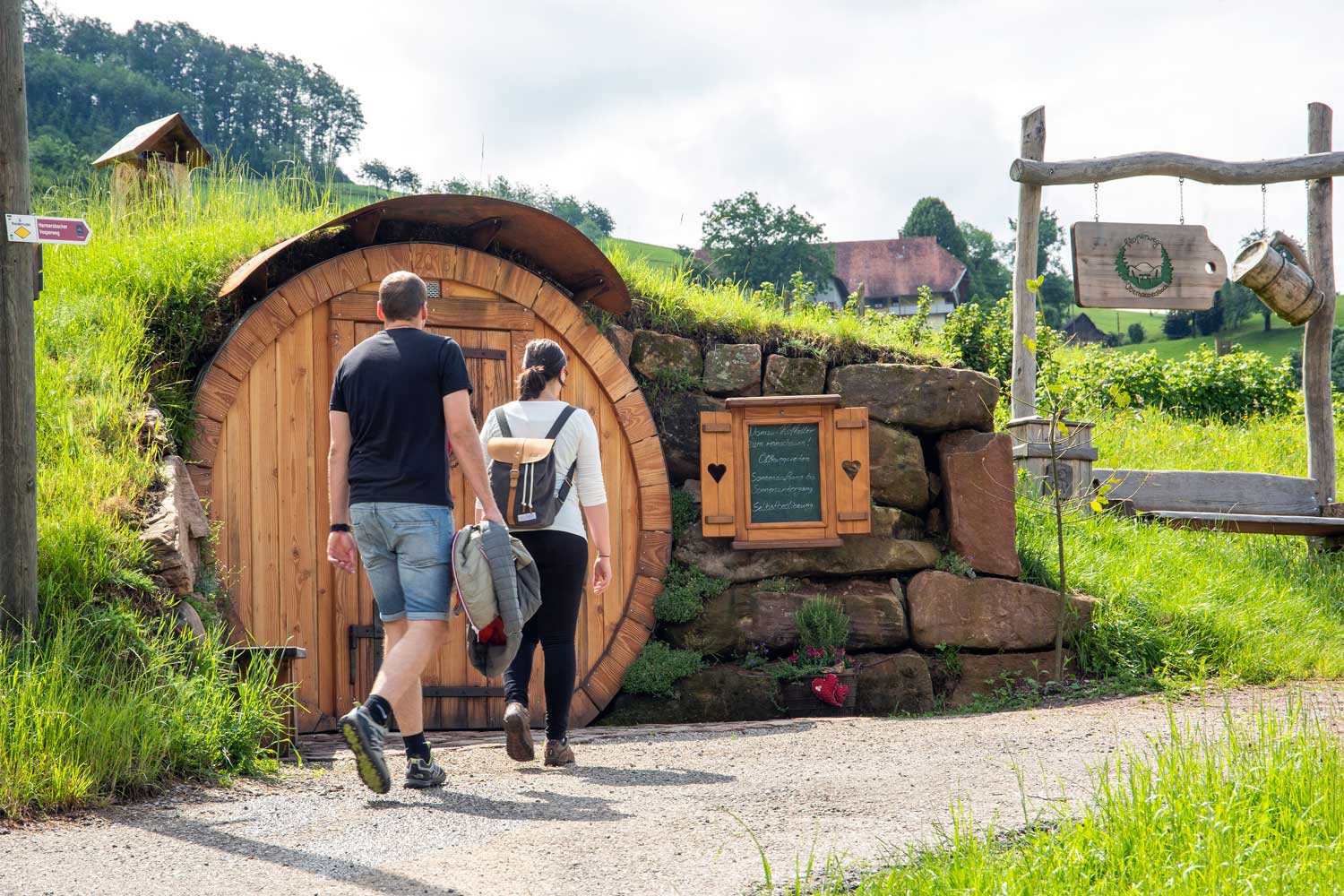 Zwei Wandernde laufen an einer runden Holztür vorbei