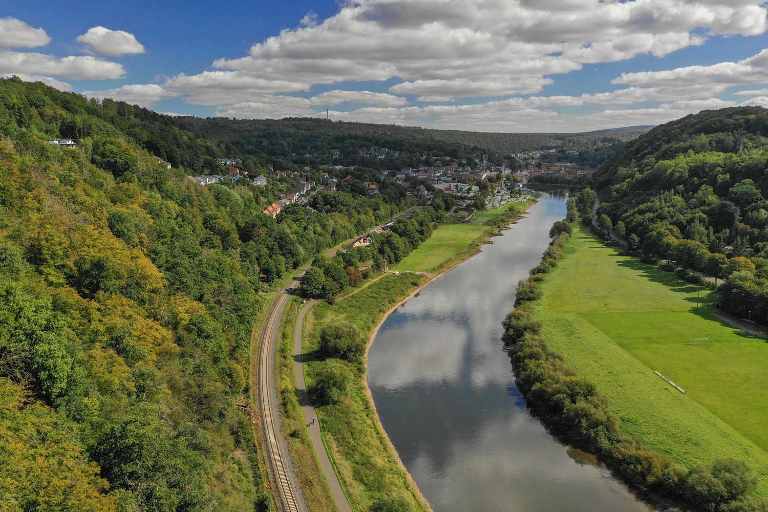 Vogelperspektive auf einen Fluss, Wald und eine Stadt im Hintergrund
