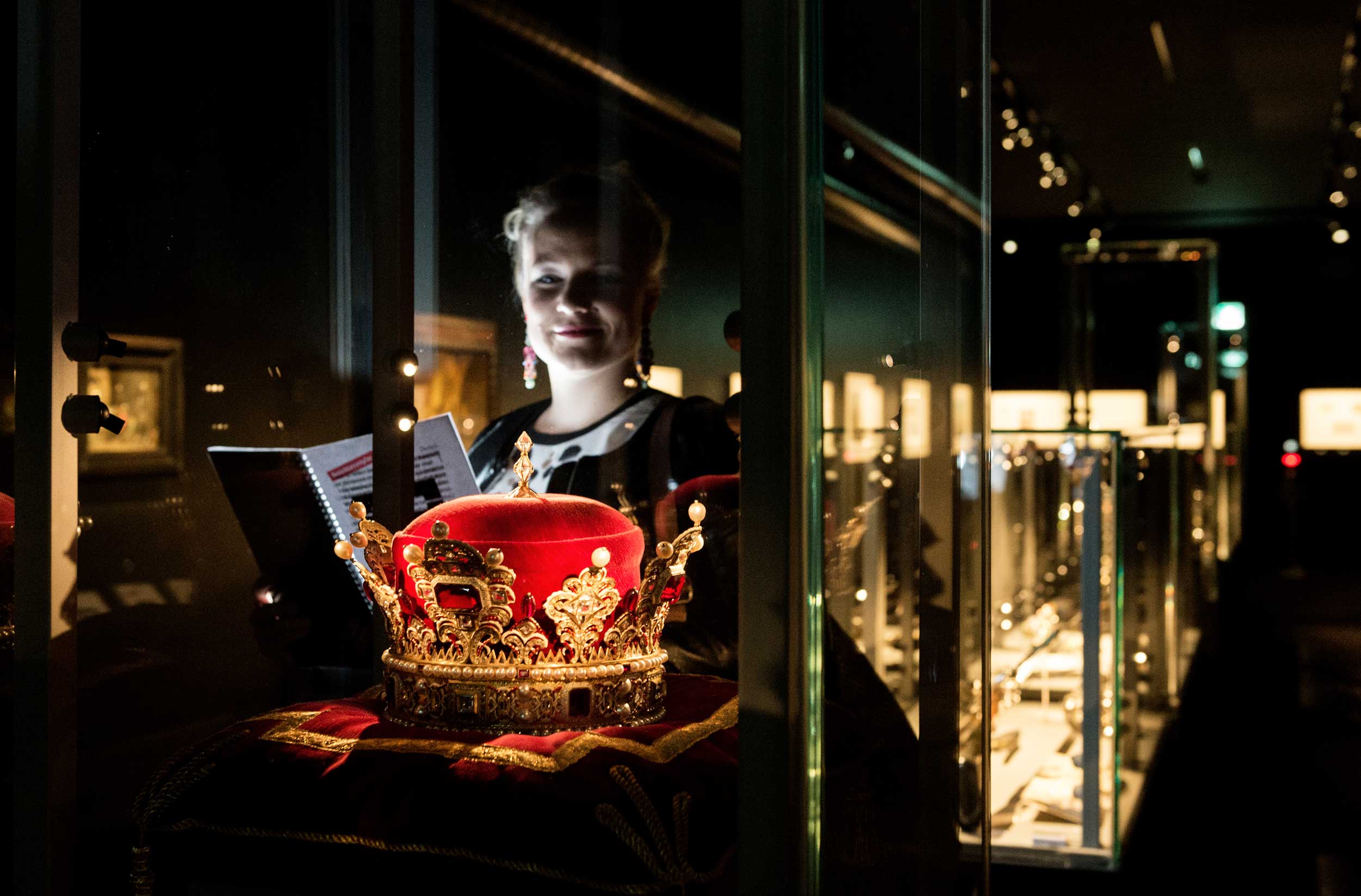Eine Frau schaut auf eine Krone in einer Glasvitrine