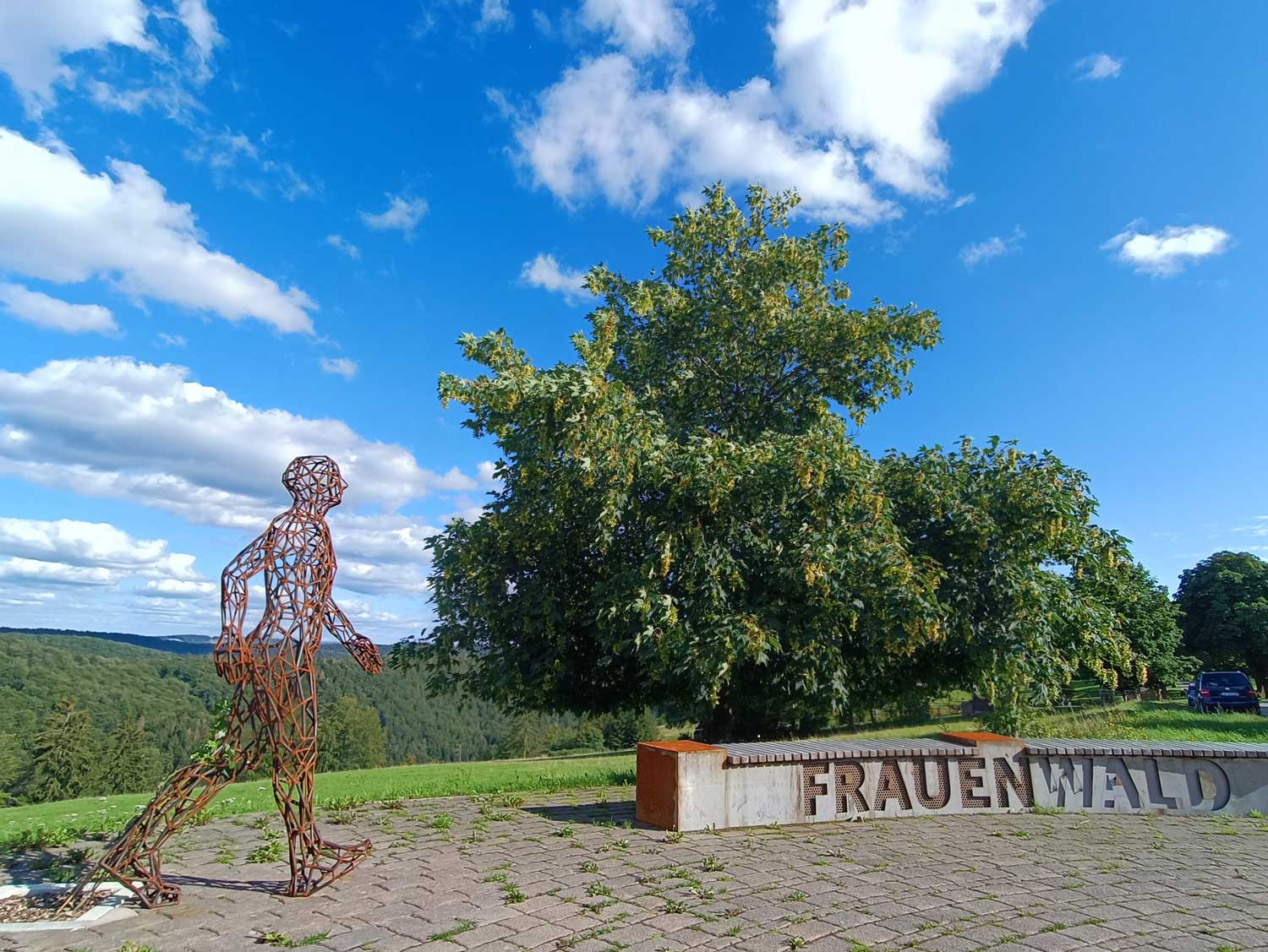 Eine Kunstfigur: Ein Mann aus Metall und eine Bank mit der Aufschrift Frauenwald