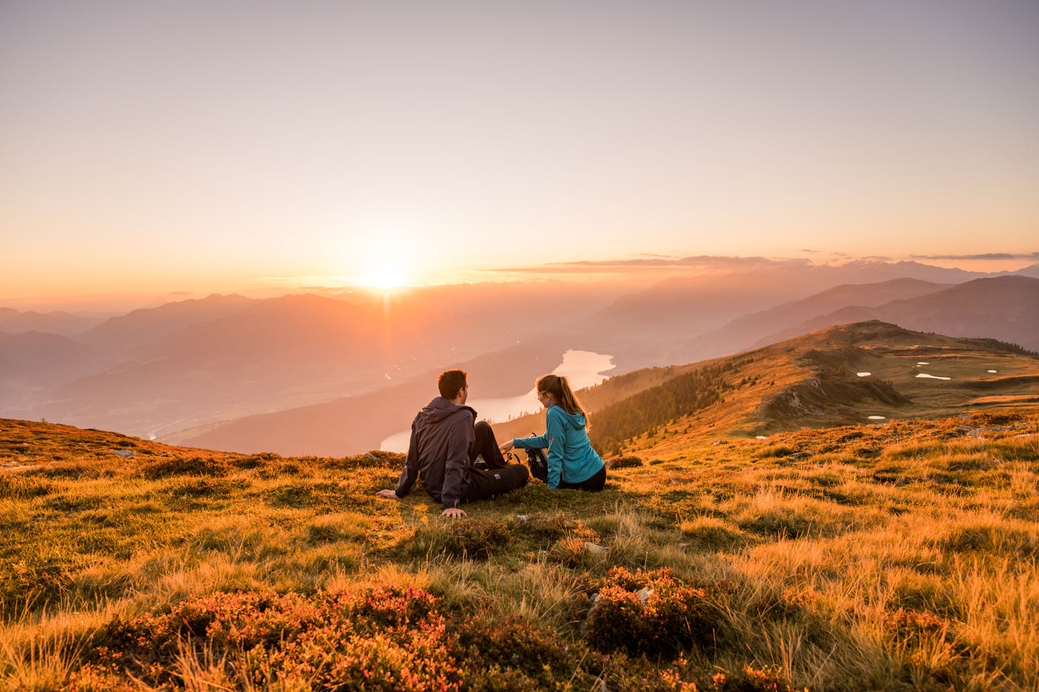 Zwei Wanderer machen Pause in der Abendsonne mit Blick auf einen See