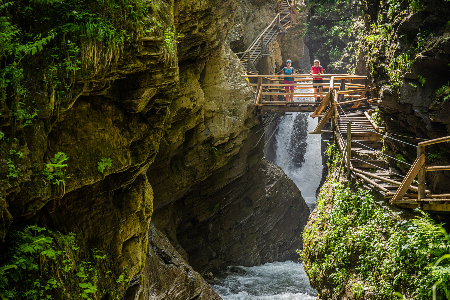 Schlucht mit Wasserfall und Brücke auf der zwei Personen stehen