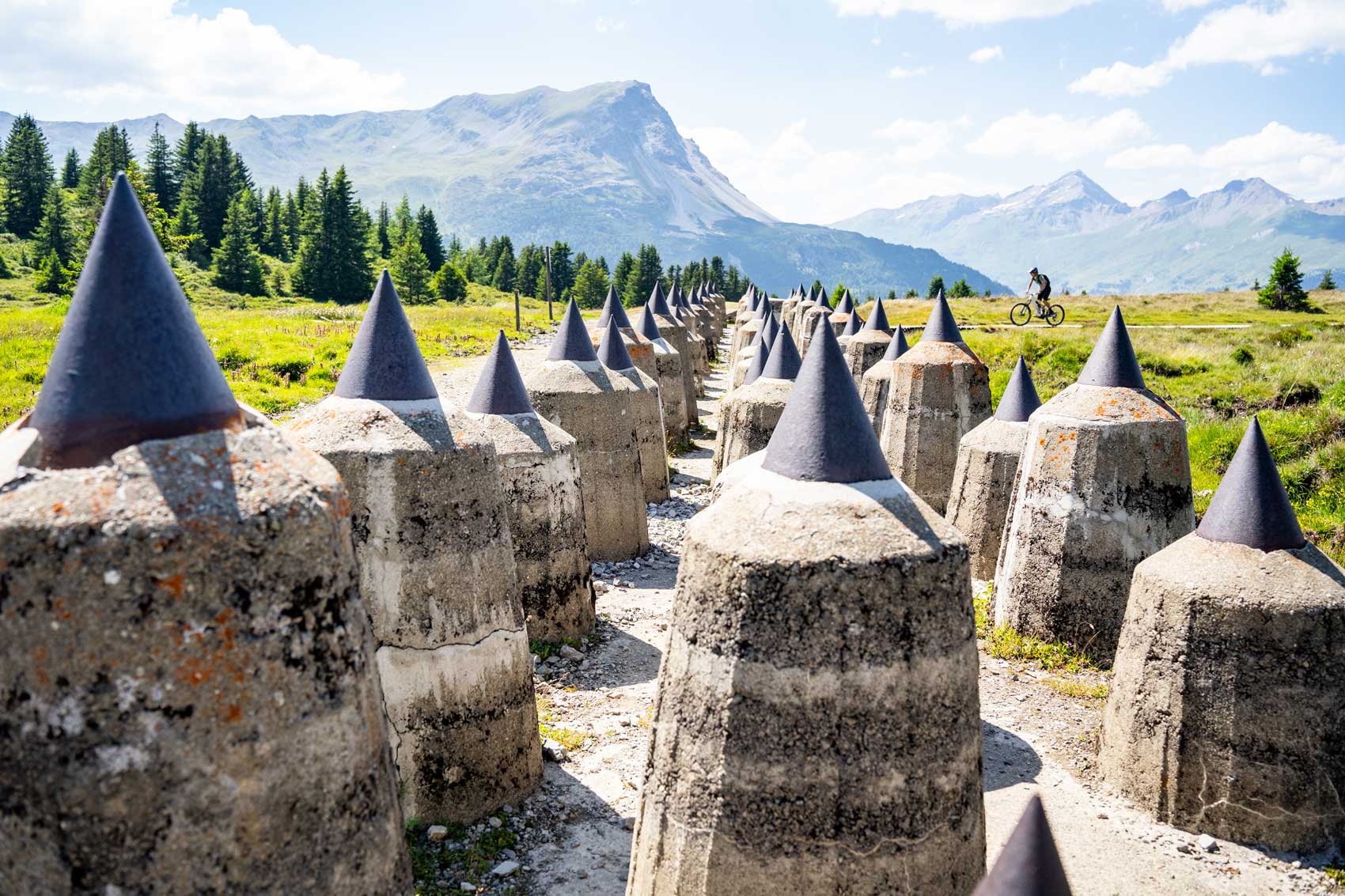 Ehemaligen Panzersperren in einer Berglandschaft, im Hintergrund ein Fahrradfahrer