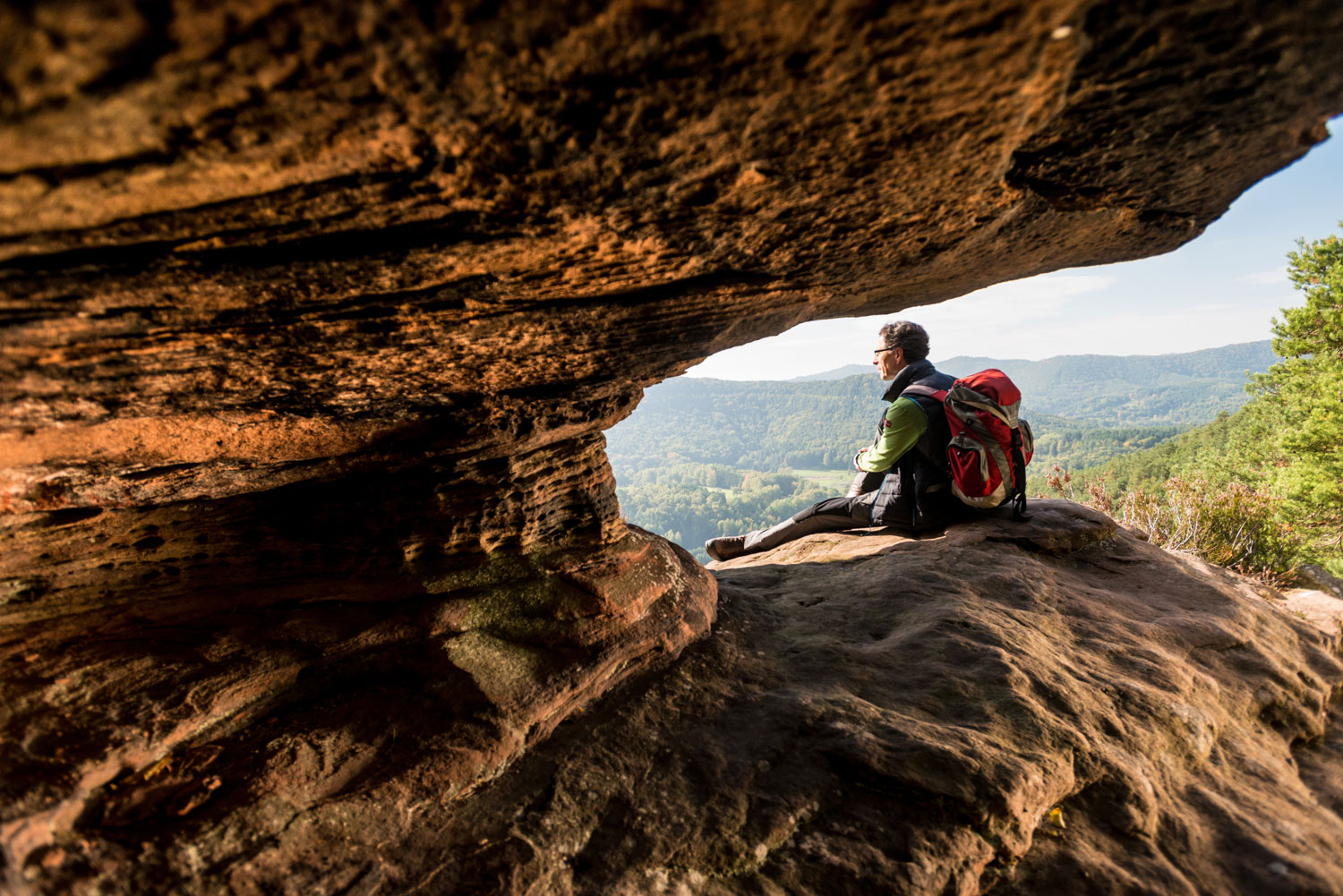 Wanderer sitzt in Felsöffnung und blickt in die Weite