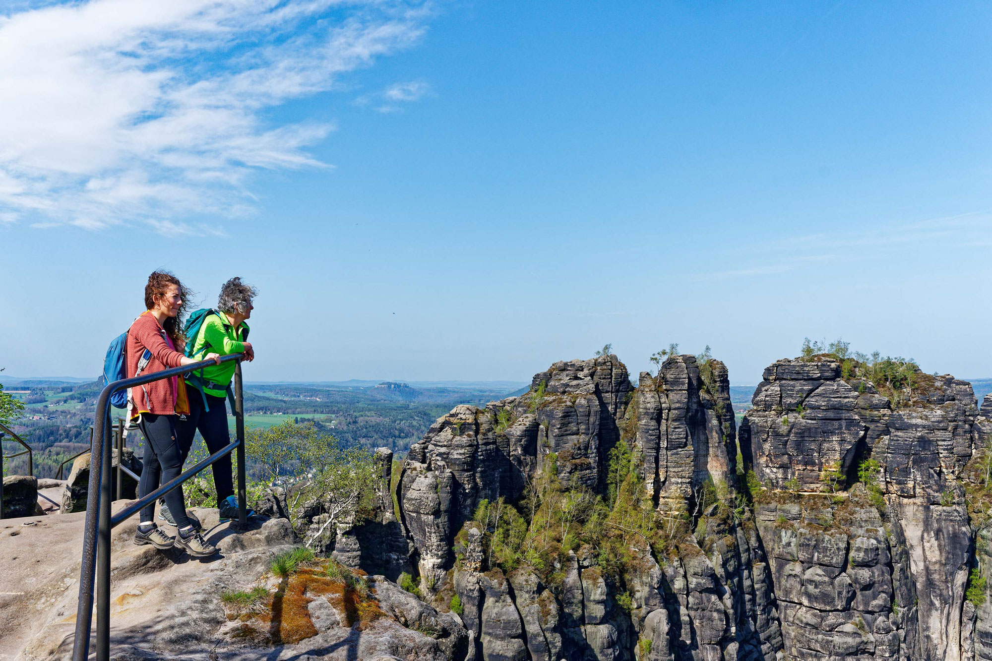 Zwei Wandernde auf einer Felskanzel blicken auf weitere Felsspitzen