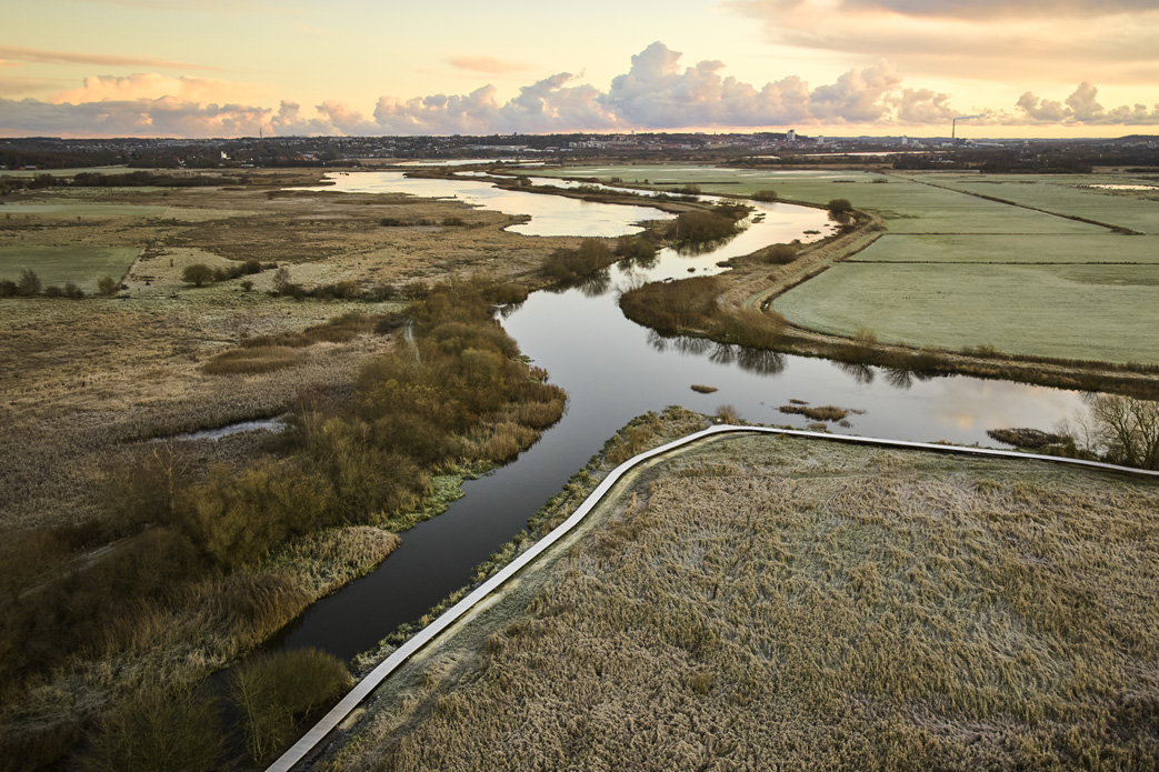 Blick auf einen Flusslauf in flacher Landschaft im Abendlicht