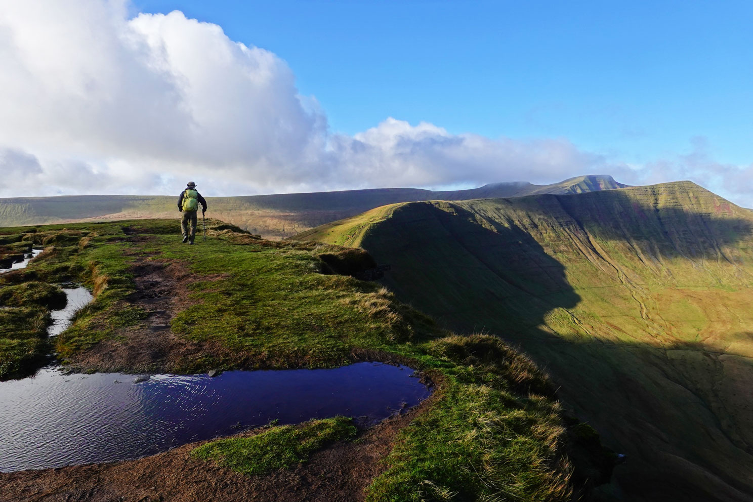 Eine zerklüftete grüne Landschaft, ein Wanderer auf dem Weg in die Weite Ebene