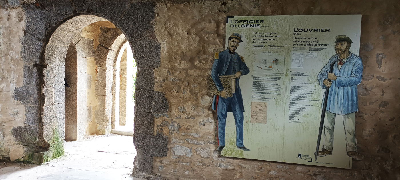 Im inneren eines steinernen Gebäudes fällt Licht durch einen runden Eingang, eine große Infotafel an der Wand