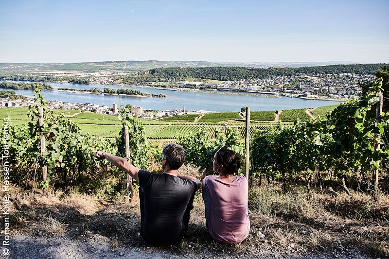 Ein Paar sitzt und blickt auf einen Weinhang vor ihnen.