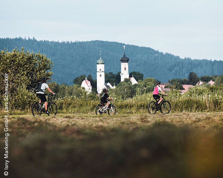 Radfahrende vor grünen Hügeln, im Hintergrund zwei Kirchtürme