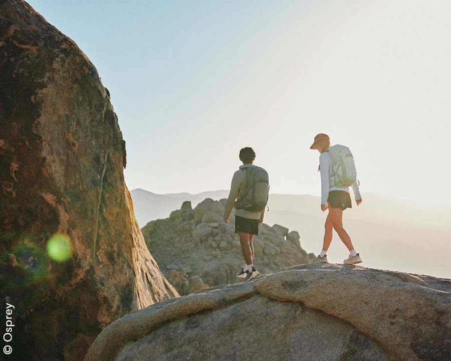 Zwei Wandernde gehen über einen Felsen bei tiefstehender Sonne