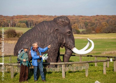 Zwei Wandernde am Geoparkzentrum Groß-Ziehen mit Mammutstatue