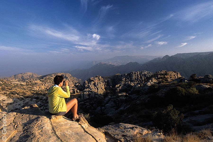 Eine Person sitzt mit einem Fernglas vor einer riesigen zerklüfteten Felslandschaft