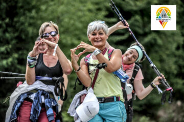 Drei Frauen mit Wanderrucksack und Trekkingstöcken lachen in die Kamera und zeigen Herzen mit den Händen
