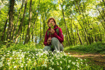 Lächelnde Frau hockt an einem Waldweg und riecht an einer Blüte