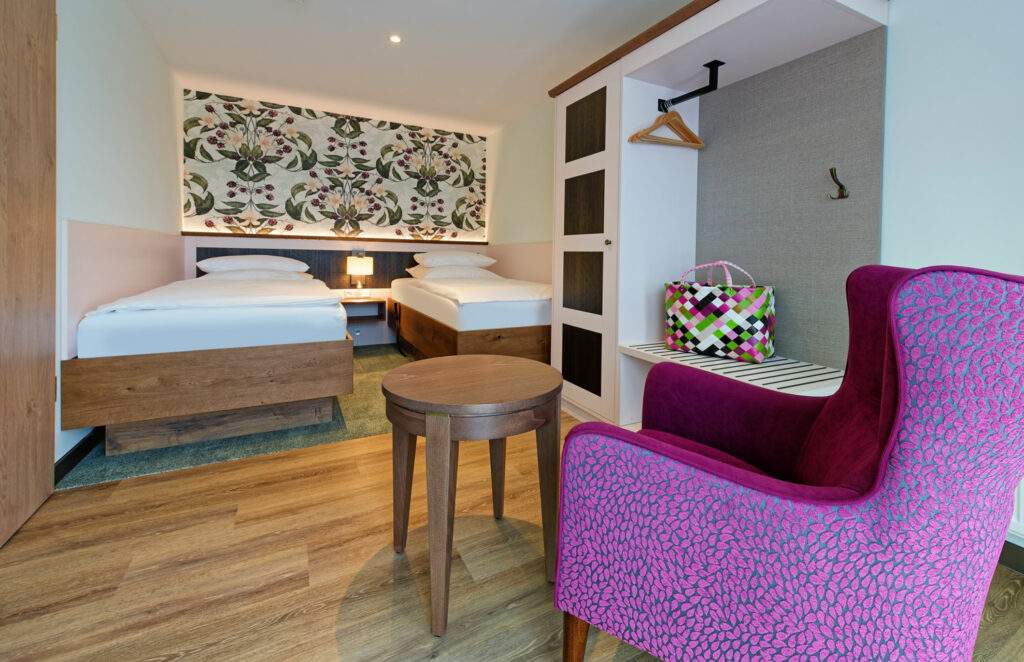 Hotelzimmer mit Bett und pinkem Lesesessel auf Holzfußboden