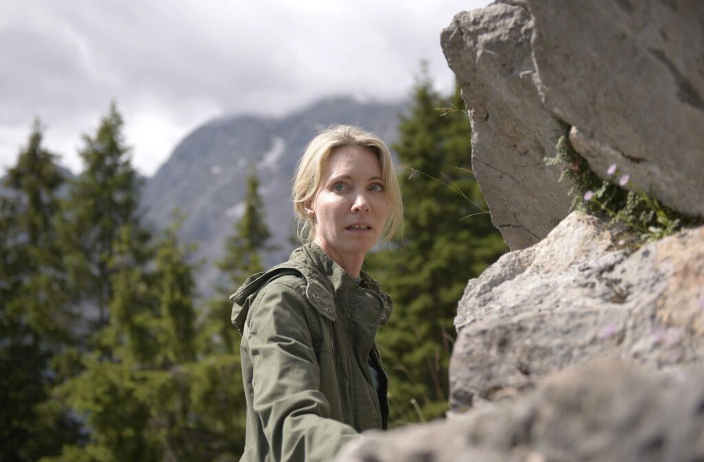 Eine Frau in alpiner Kulisse blickt besorgt über ihre Schulter zurück