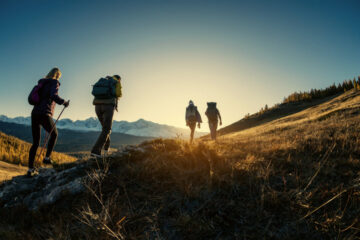 Die Silhouetten von vier Wandernden im gleißend hellen Abendlicht in einer Bergkulisse