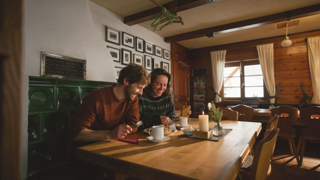 Zwei Wandernde sitzen an in einer klassischen Almstube und genießen Kaiserschmarn.