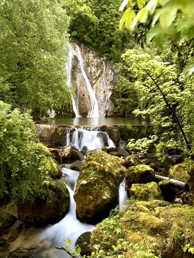 Ein Wasserfall mit mehreren Kaskaden im Grünen und mit moosbewachsenen Steinen