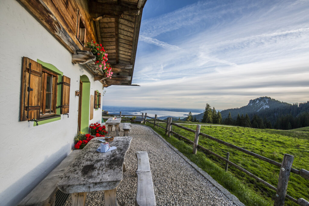 Hauswand mit Holz und Fensterläden, Tisch und Bänken, einem Zaun und Bergblick