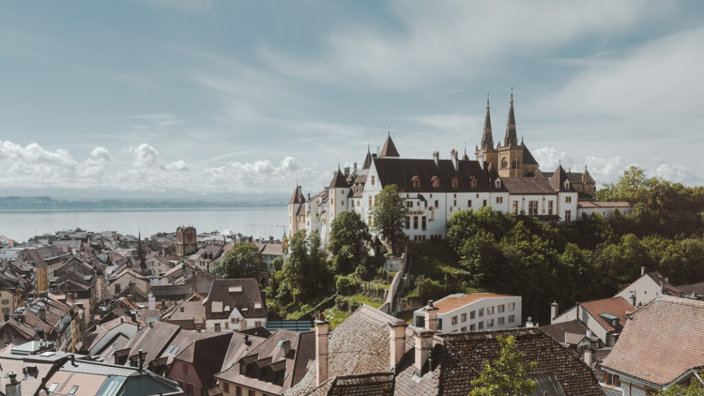 Ein imposantes Schloss über den Häusern eines Ortes, im Hintergrund ein See
